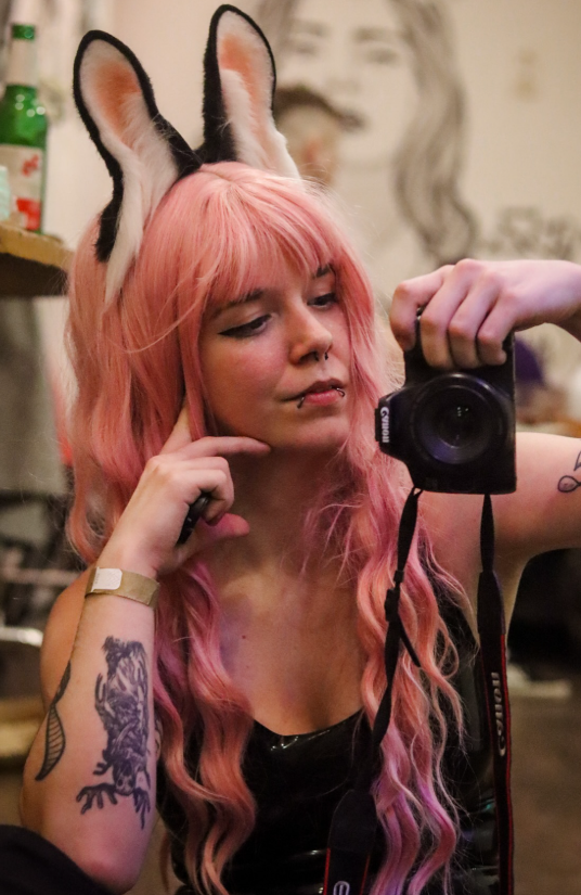 LittleAxl699 fotí s digitálním fotoaparátem v ruce, má na sobě sexy černý top a růžovou paruku.