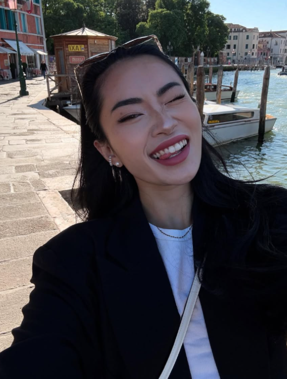 Asia Nina se fotí u řeky a má na sobě bílou košili a černé sako.