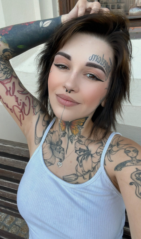 Počmáraná Dryáda fotící se v sexy modrém tílku s rukou na hlavě.