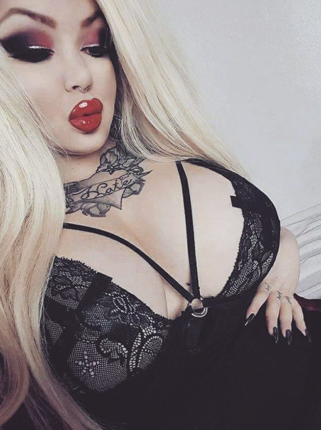 Rebecca Randall taking a picture while dressed in a sexy low-cut dress with her hand on her waist.