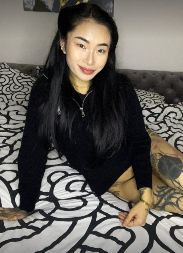 Asia Nina fotí, zatímco sedí na posteli a oblečená v sexy černém krátkém oblečení