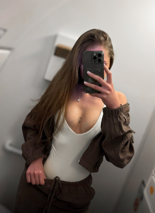 Alžběta oblečená v sexy bílém topu, hnědé bundě a hnědých kalhotách